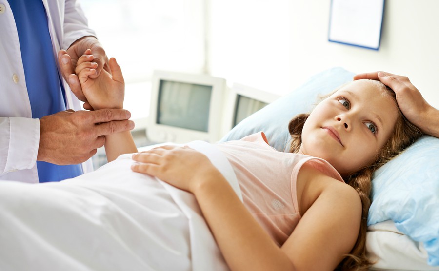 smiling-girl-lying-in-bed-in-hospital-surrounded-by-doctors