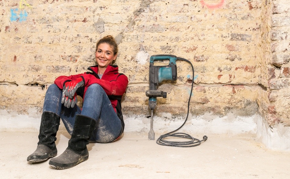 smiling craftswoman sitting on the floor against brick wall needing French property renovation