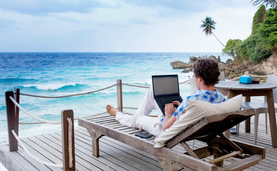 man-with-laptop-and-mobile-phone-running-remotely-on-colorful-beach-of-island-among-the-palms-cafe