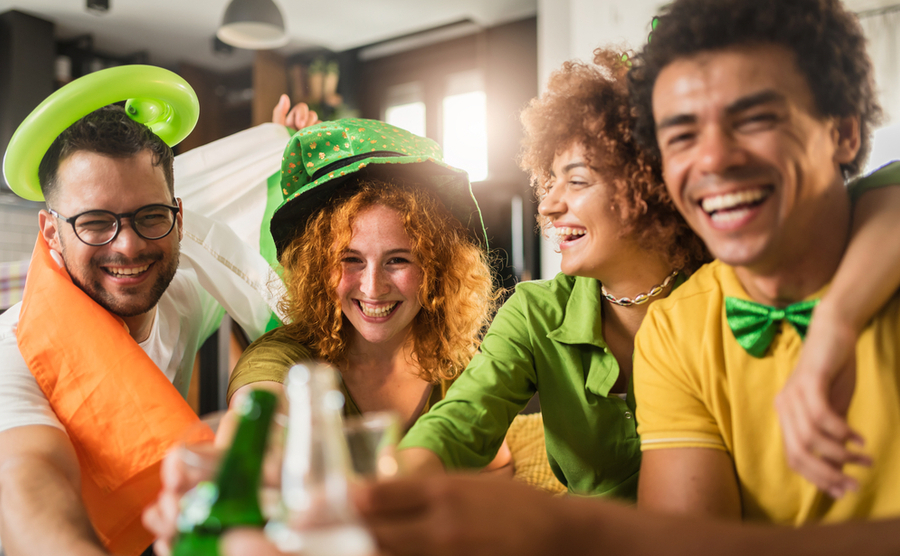 Friends smiling and clinking glasses while wearing green colours on St. Patrick's Day