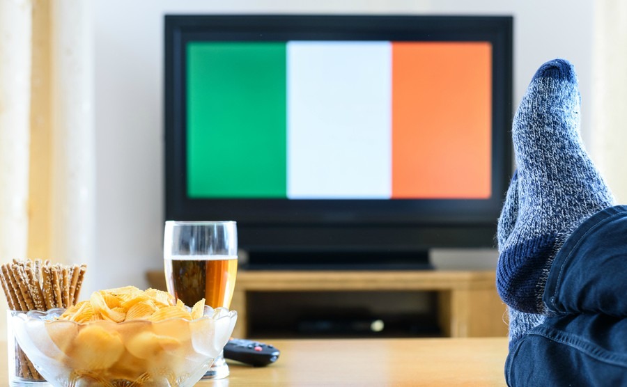 man-watching-irishireland-flag-on-tv-screen-with-legs-on-table-stock-photo