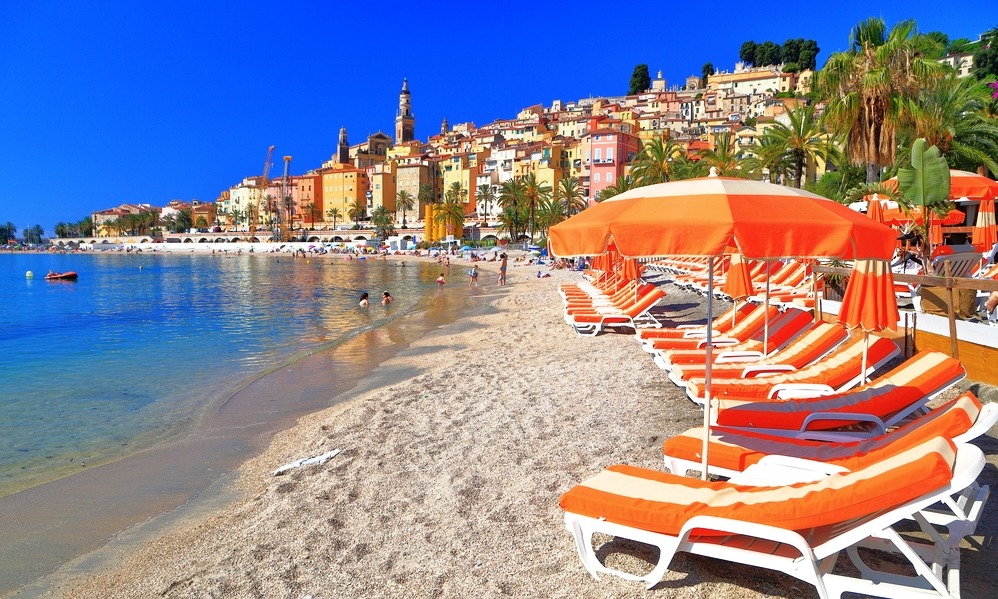 Beach chairs and umbrellas along sandy beach in Menton, French Riviera, France