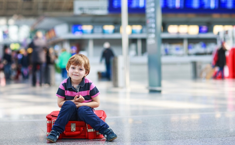 Blond boy of 4 years sitting on suitcase at the airport