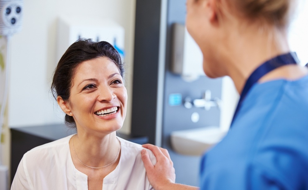 Female Patient Being Reassured By Doctor In Hospital Room