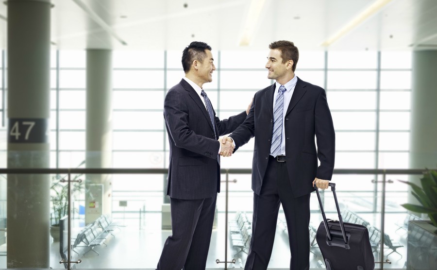 two-businessmen-one-asian-and-one-caucasian-shaking-hands-and-smiling-at-modern-airport