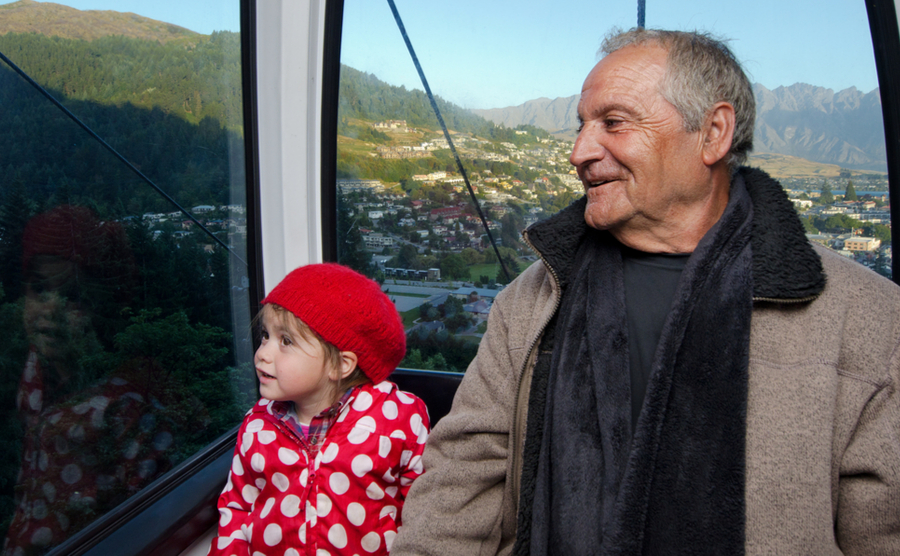 Grandfather (male age 70) and his granddaughter (female age 05) travel by aerial tramway in Queenstown, in the south island of New Zealand. Real people. 