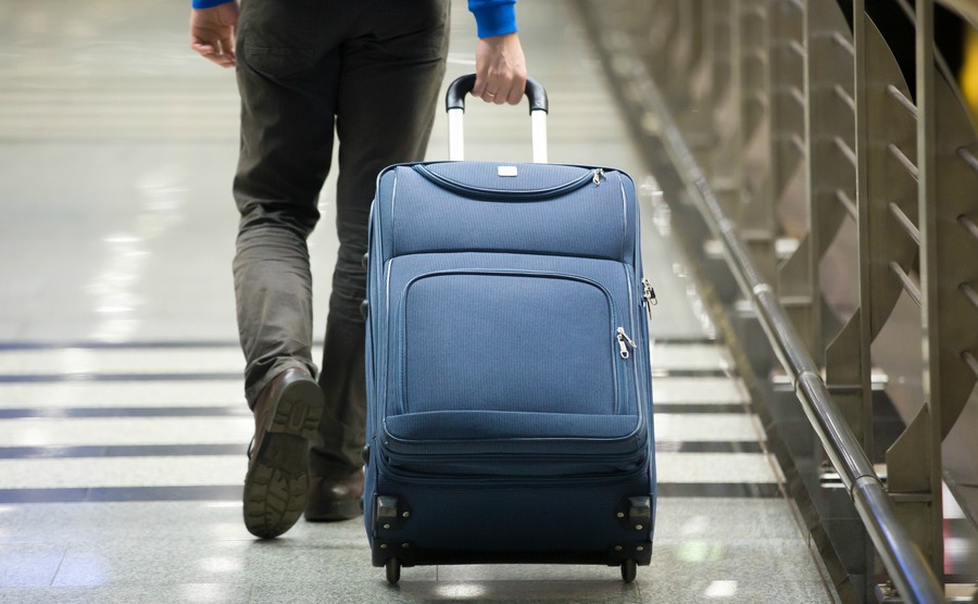 young-man-pulling-suitcase-in-modern-airport-terminal-travelling-guy-wearing-smart-casual-style-clothes-walking-away-with-his-luggage-while-waiting-for-transport-rear-view-close-up