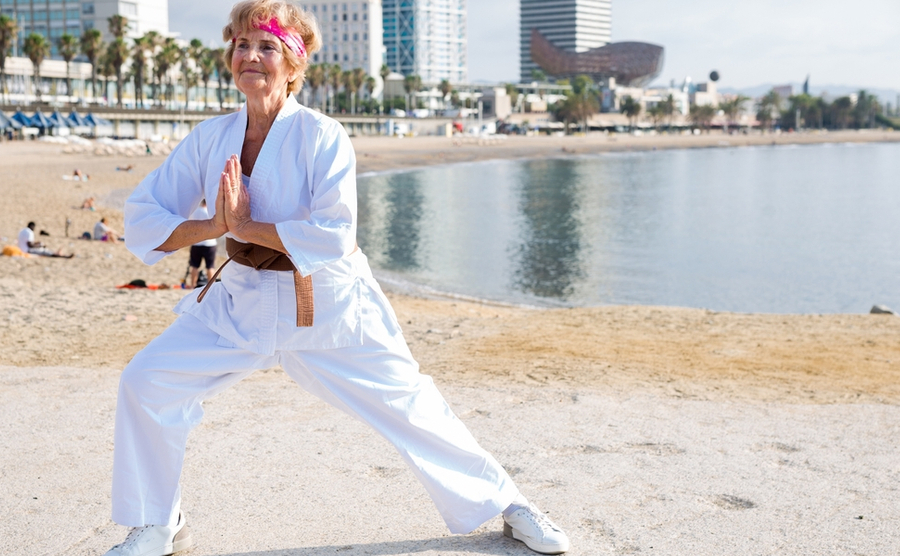 An elderly woman practices karate on the beach. Sports in Spain.